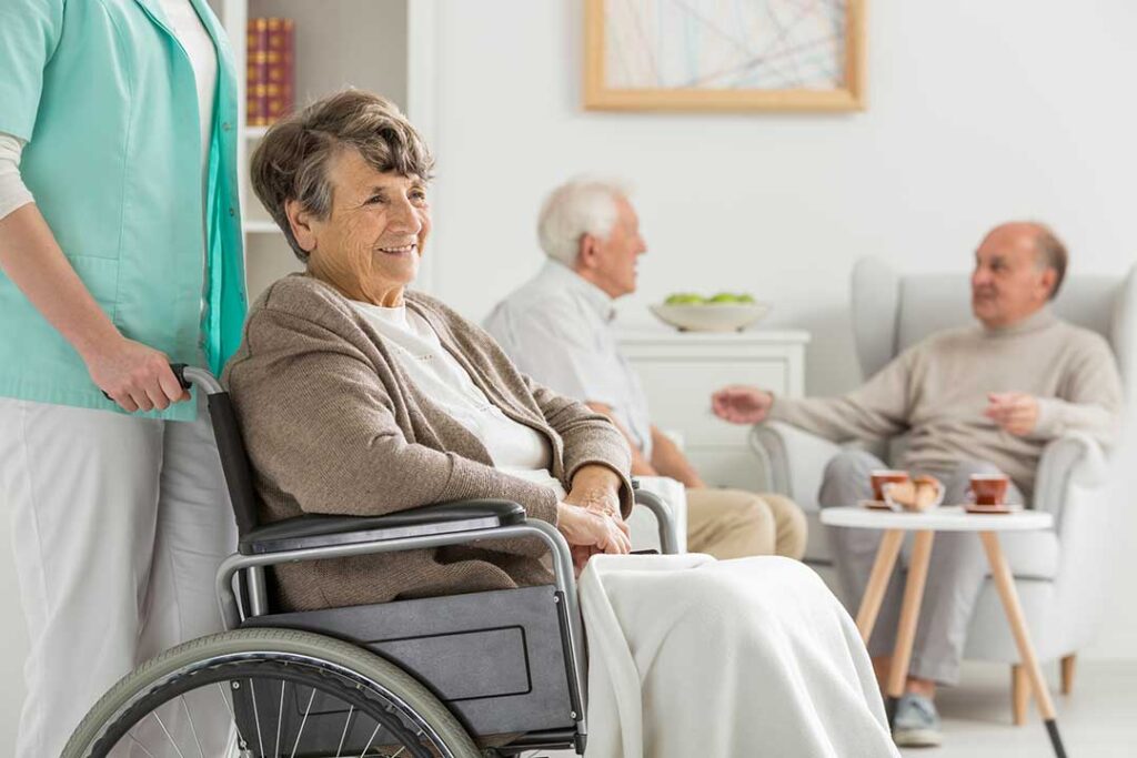 Older adults and family members talking around a kitchen table with warm sunlight through the window.